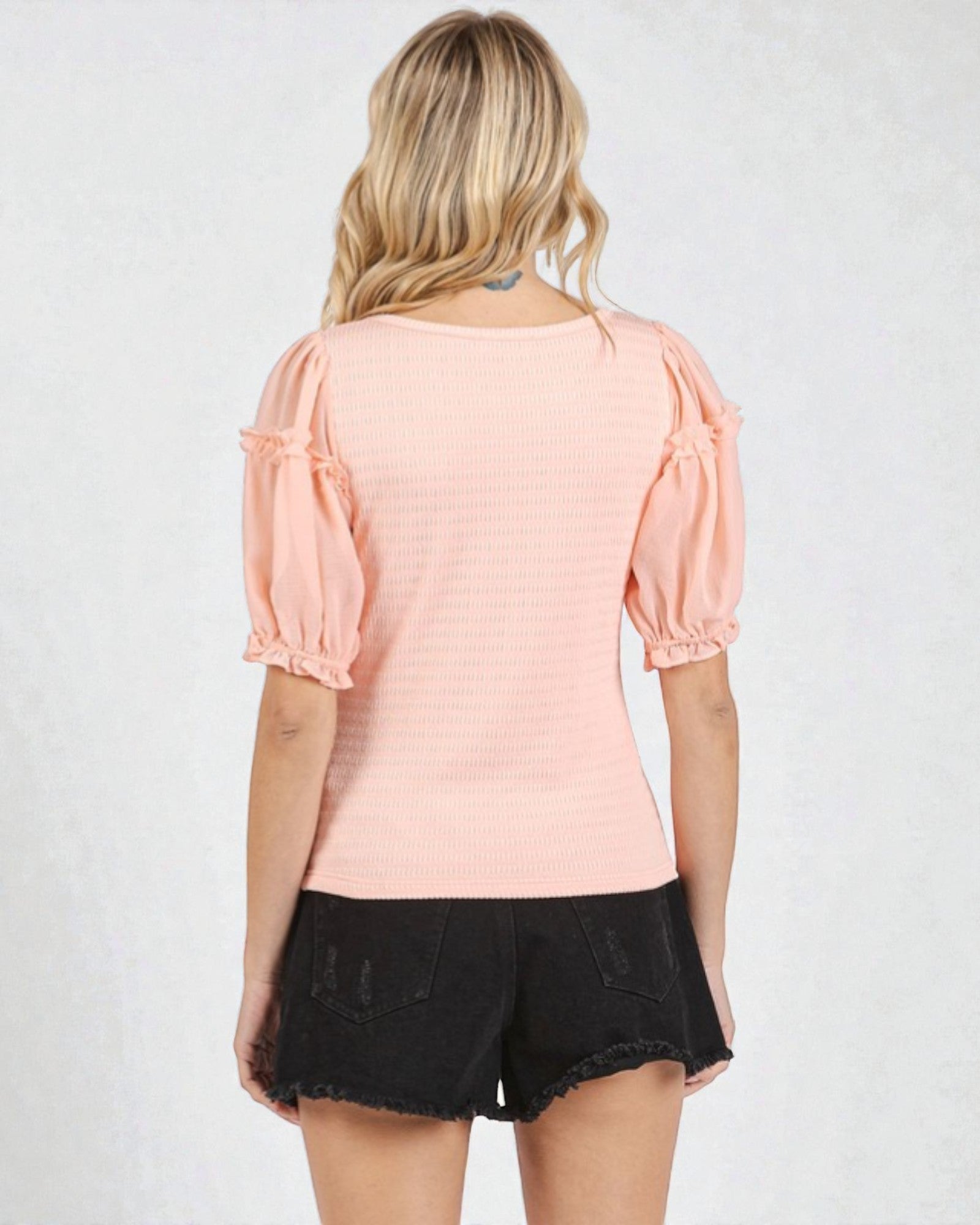 Person wearing a pink top with puff sleeves and black shorts on a white background
