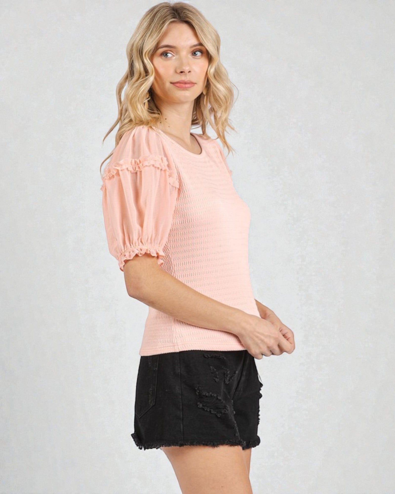 Woman wearing a pink blouse with puff sleeves and a black skirt on a light gray background