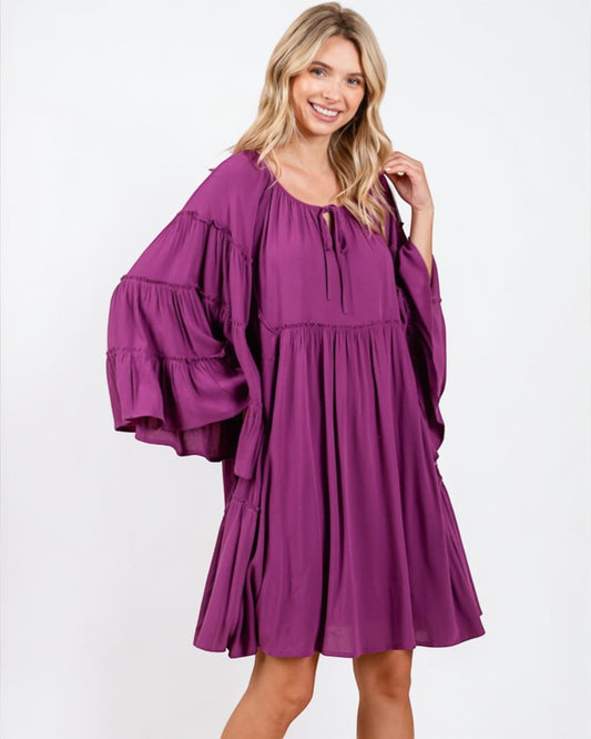 Woman wearing a purple dress with ruffled sleeves on a white background