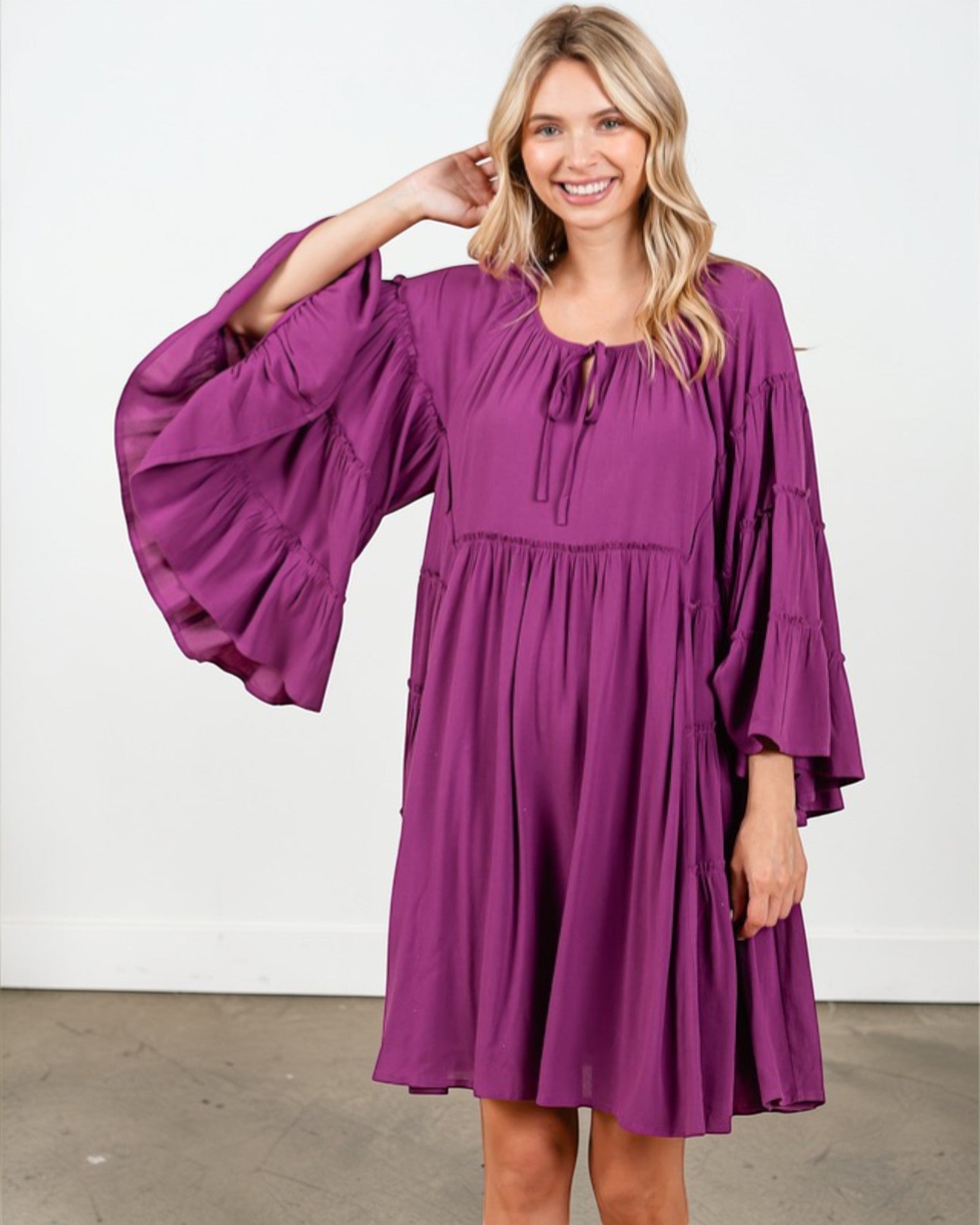 Woman wearing a purple dress with wide sleeves against a white background