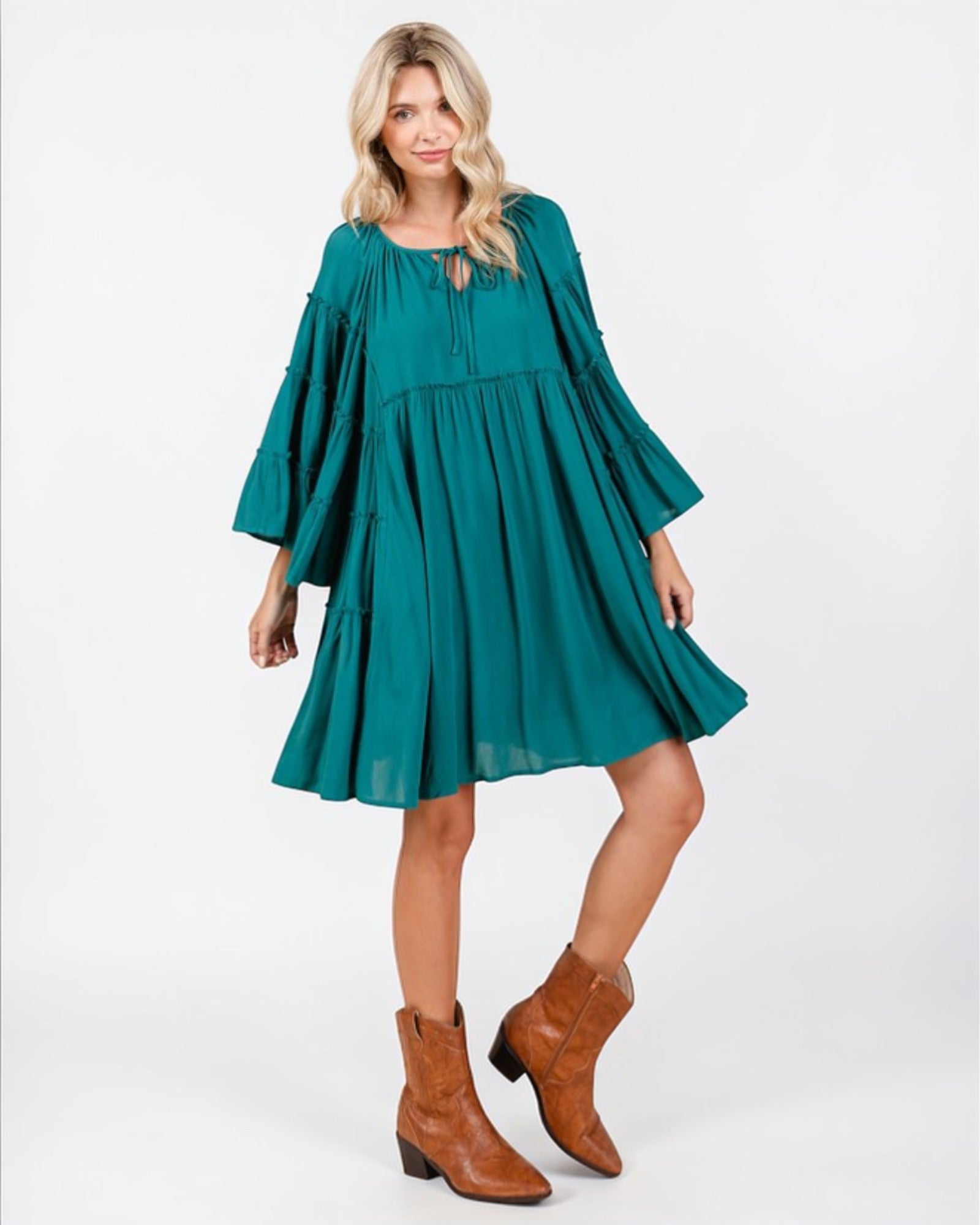 Woman wearing a teal dress with long sleeves and brown boots on a white background