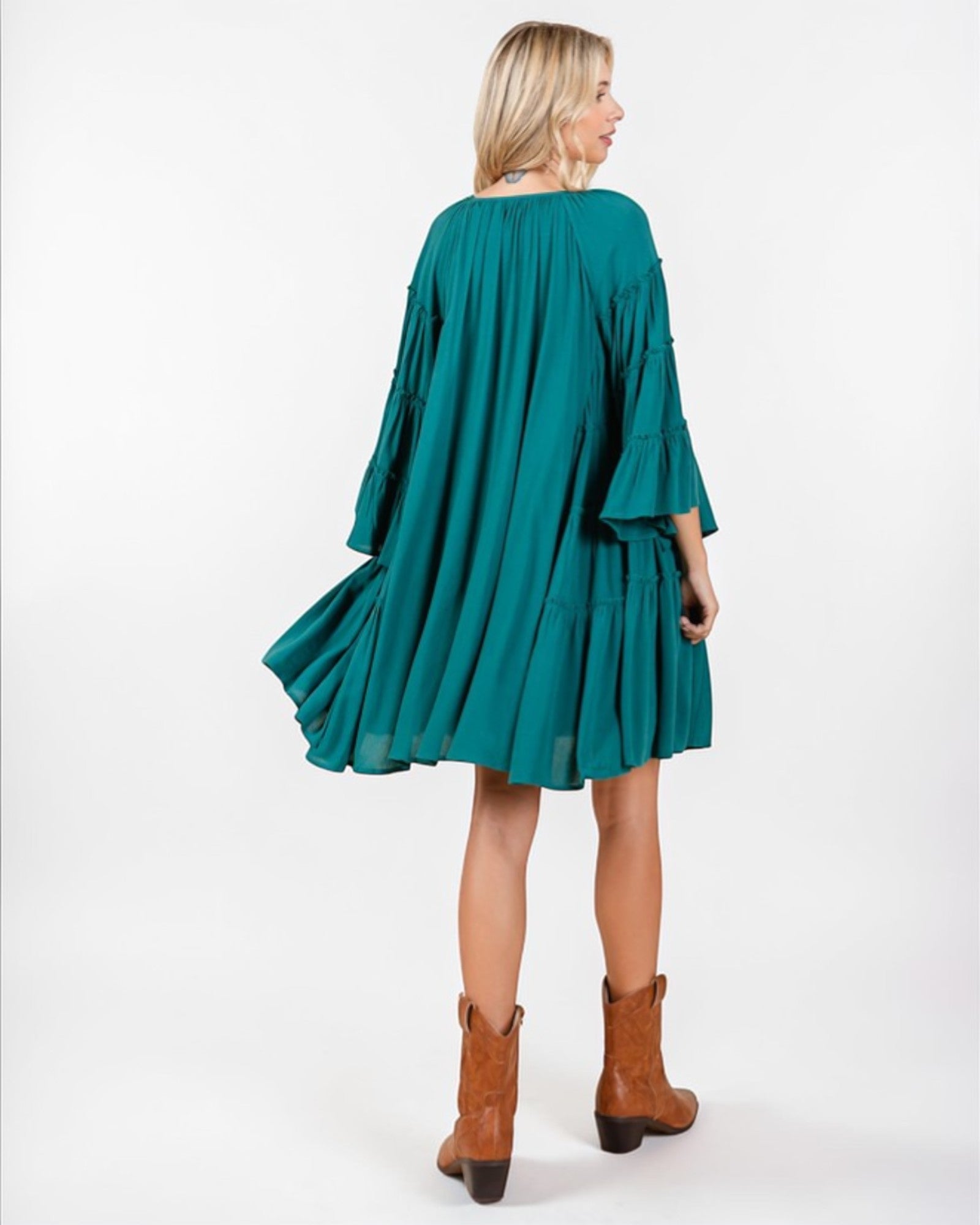 Woman wearing a teal dress and brown boots on a white background