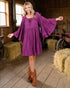Woman in a purple dress standing in a barn with hay bales.