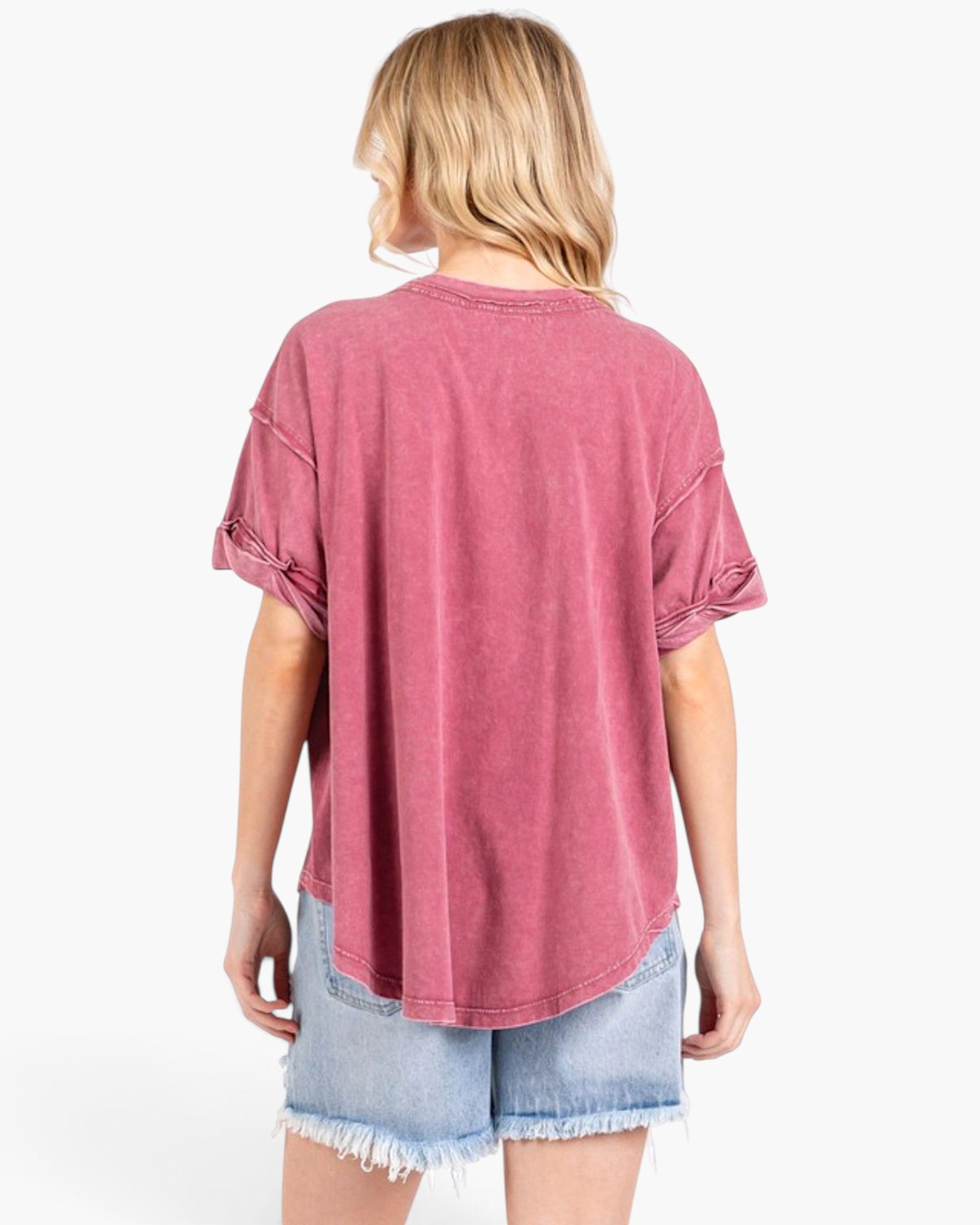 A woman shown from the back wearing a washed dusty rose short-sleeve t-shirt and light blue denim shorts against a plain white background.