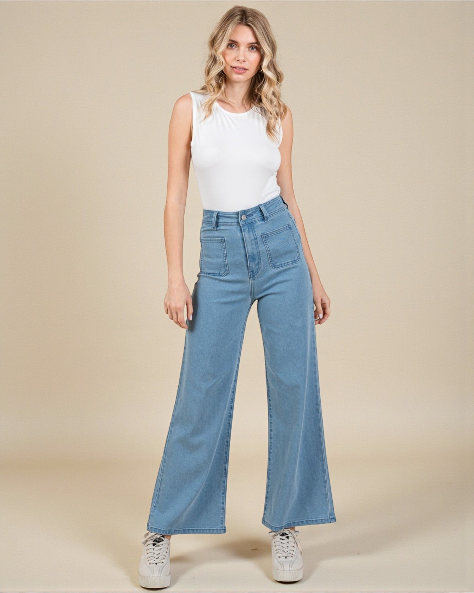 Woman wearing a white sleeveless top and blue jeans on a beige background