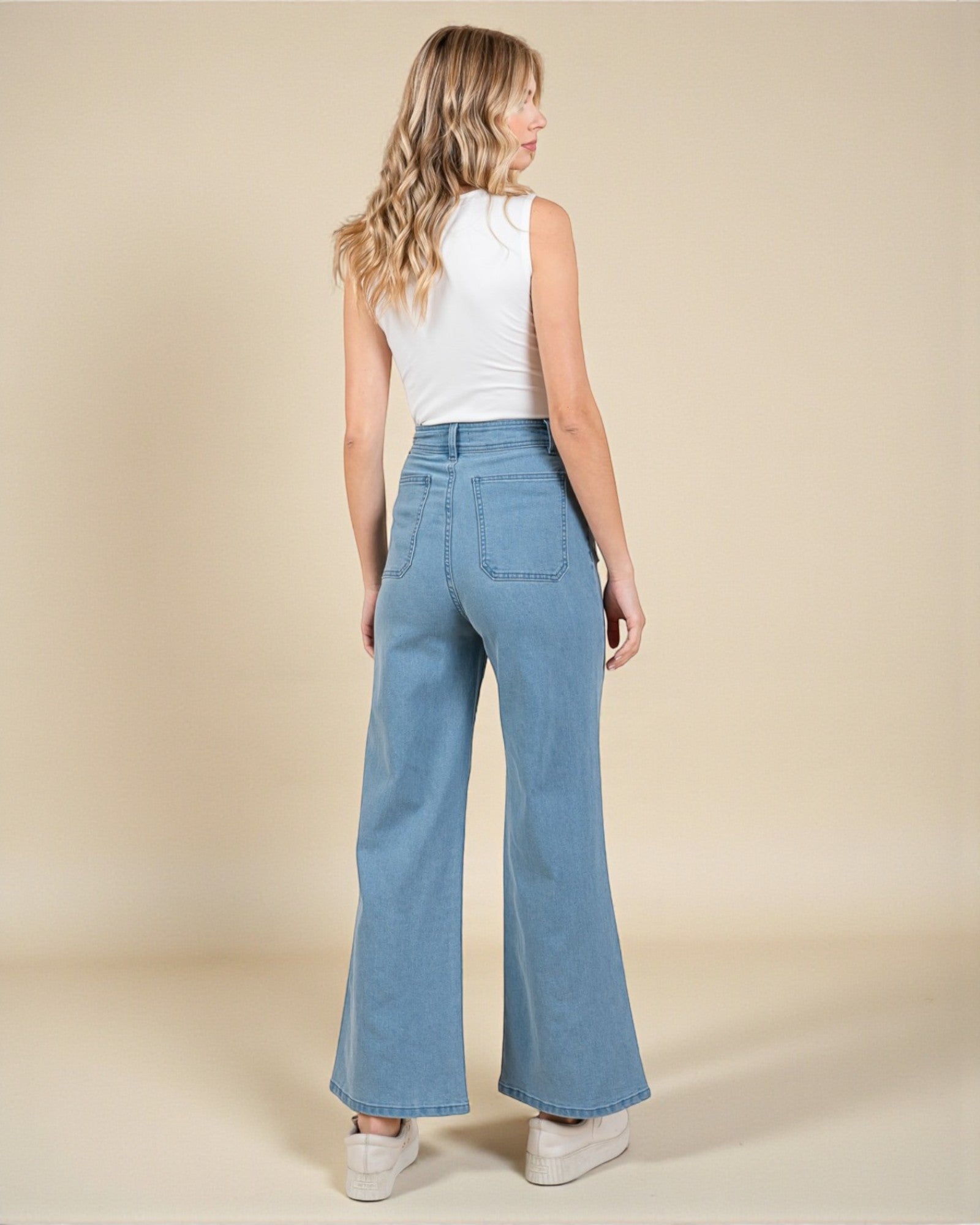 Woman wearing blue flared jeans and a white top on a beige background
