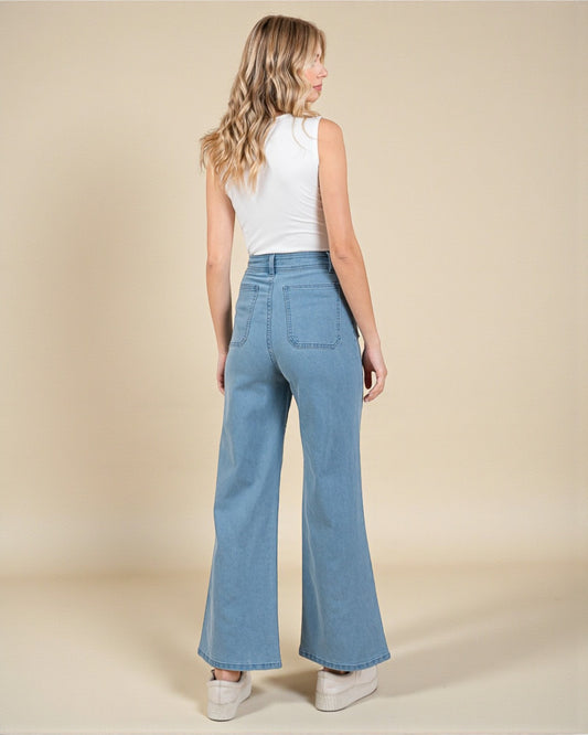 Woman wearing blue flared jeans and a white top on a beige background