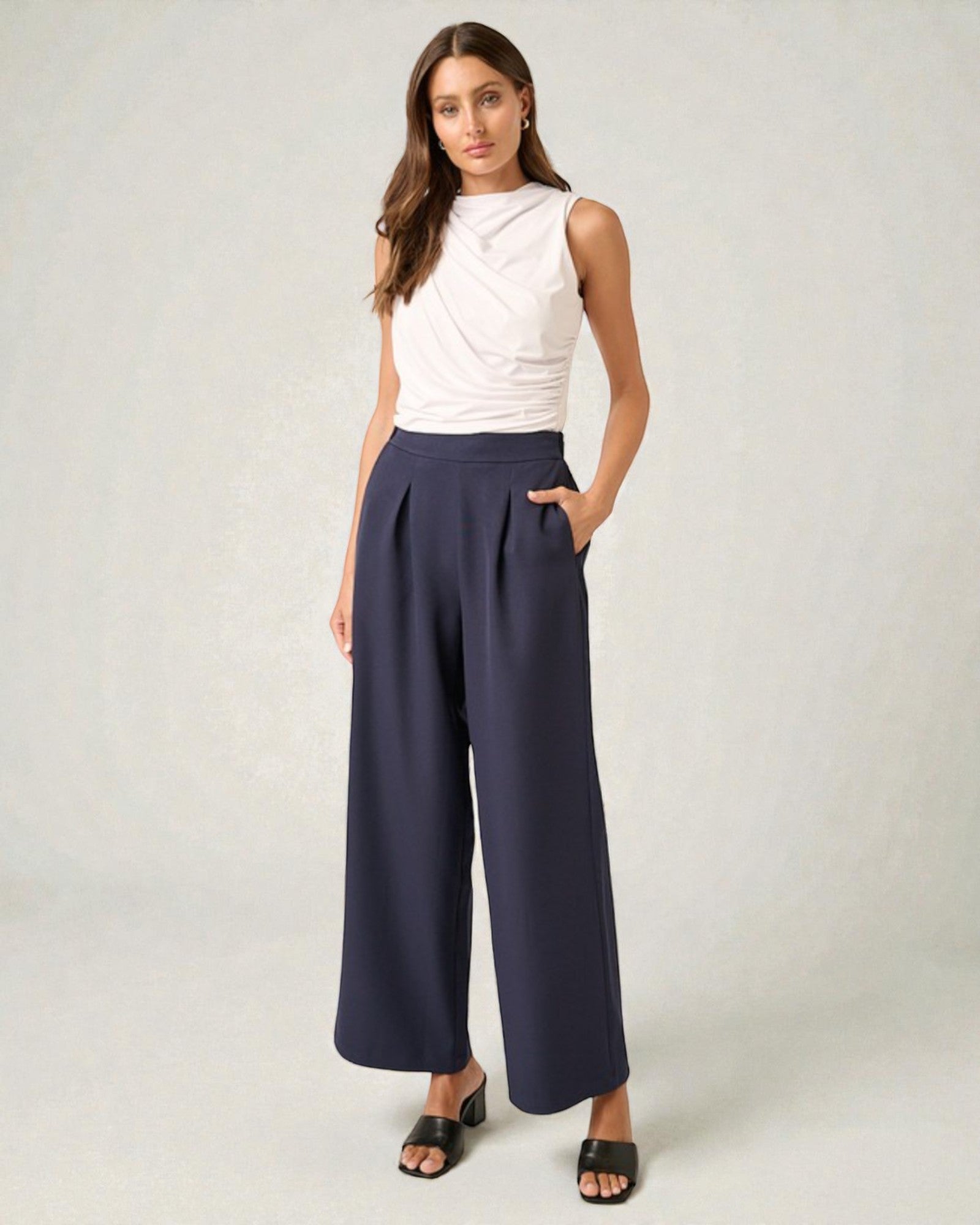 Woman wearing a white sleeveless top and navy wide-leg pants on a plain background