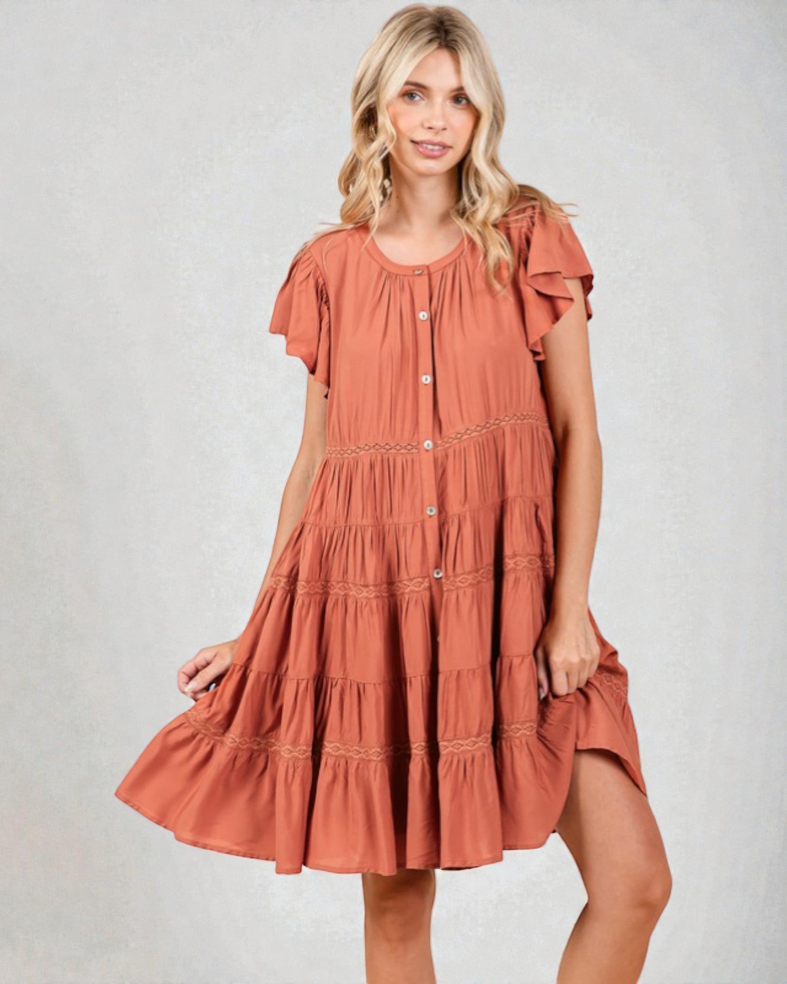 Woman wearing a tiered rust-colored dress on a plain background