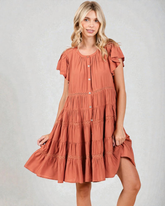 Woman wearing a tiered rust-colored dress on a plain background