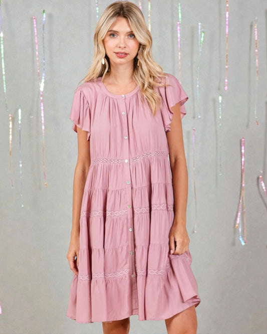 Woman wearing a pink dress with ruffled sleeves against a decorative curtain background