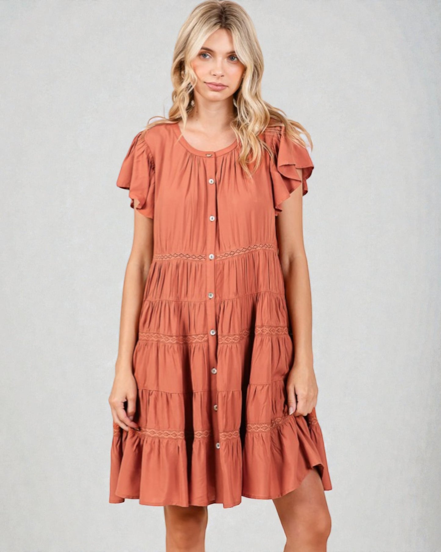 Woman wearing a rust-colored dress with ruffled sleeves on a gray background