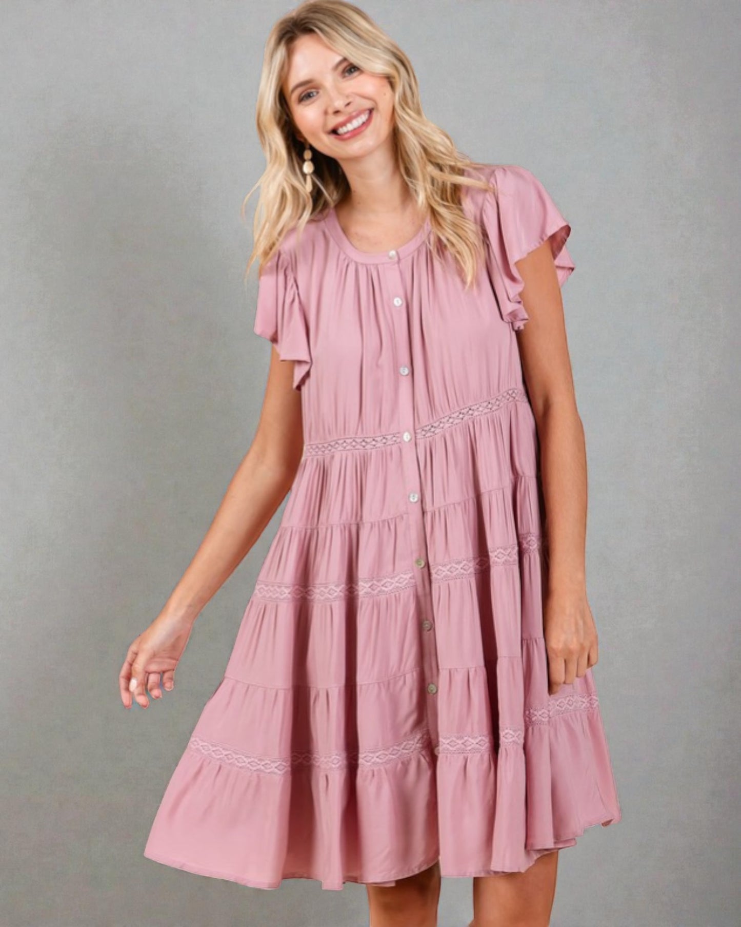 Woman wearing a pink dress with ruffled sleeves against a gray background