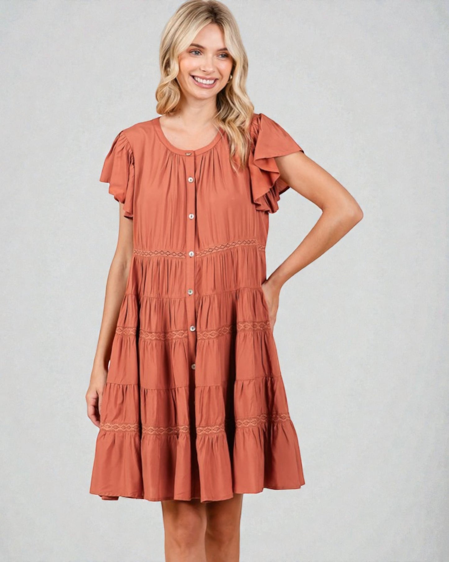 Woman wearing a rust-colored dress with ruffled sleeves on a plain background