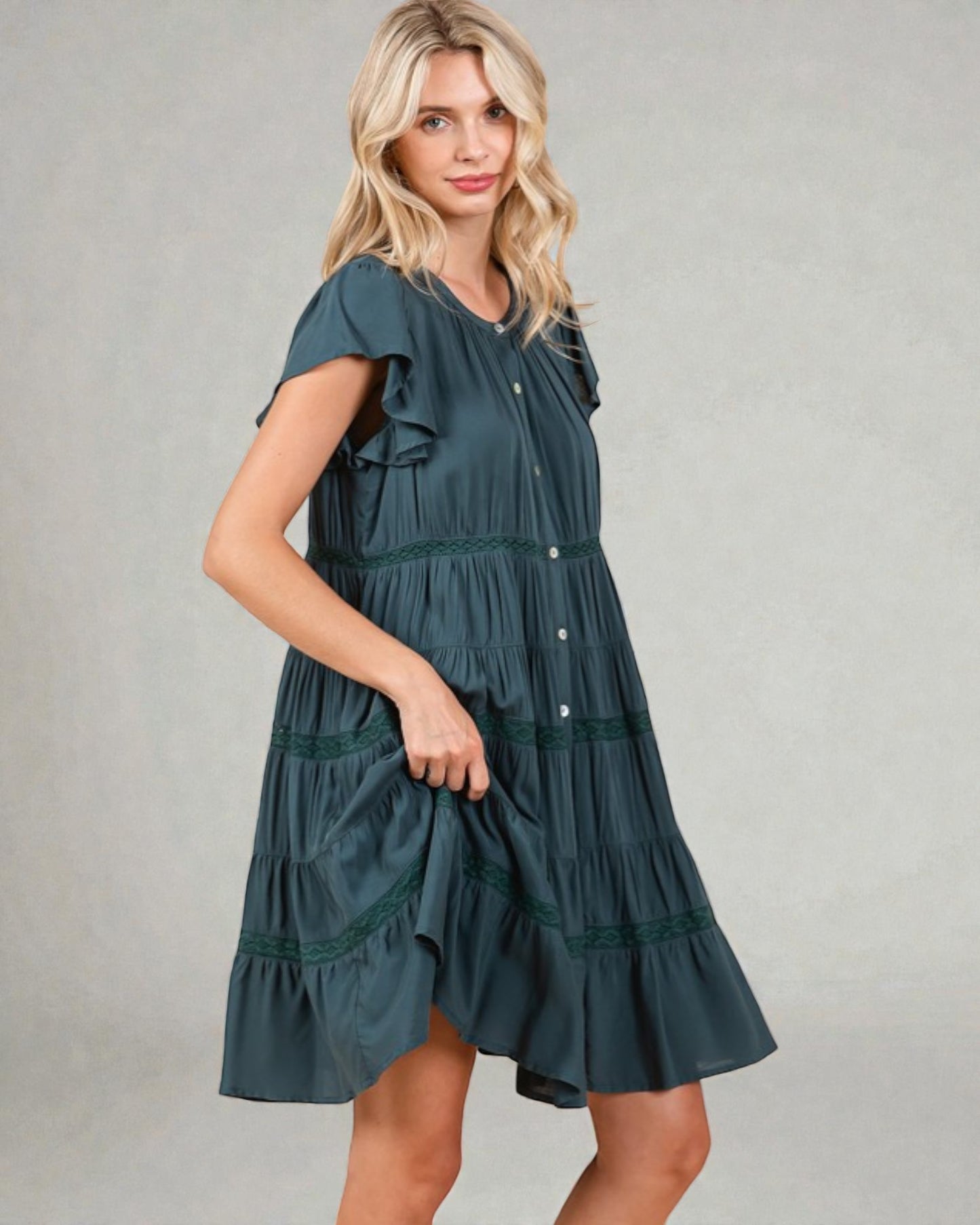 Woman wearing a teal dress with ruffled sleeves and tiered skirt on a gray background