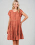 Woman wearing a rust-colored dress with ruffled sleeves on a plain background
