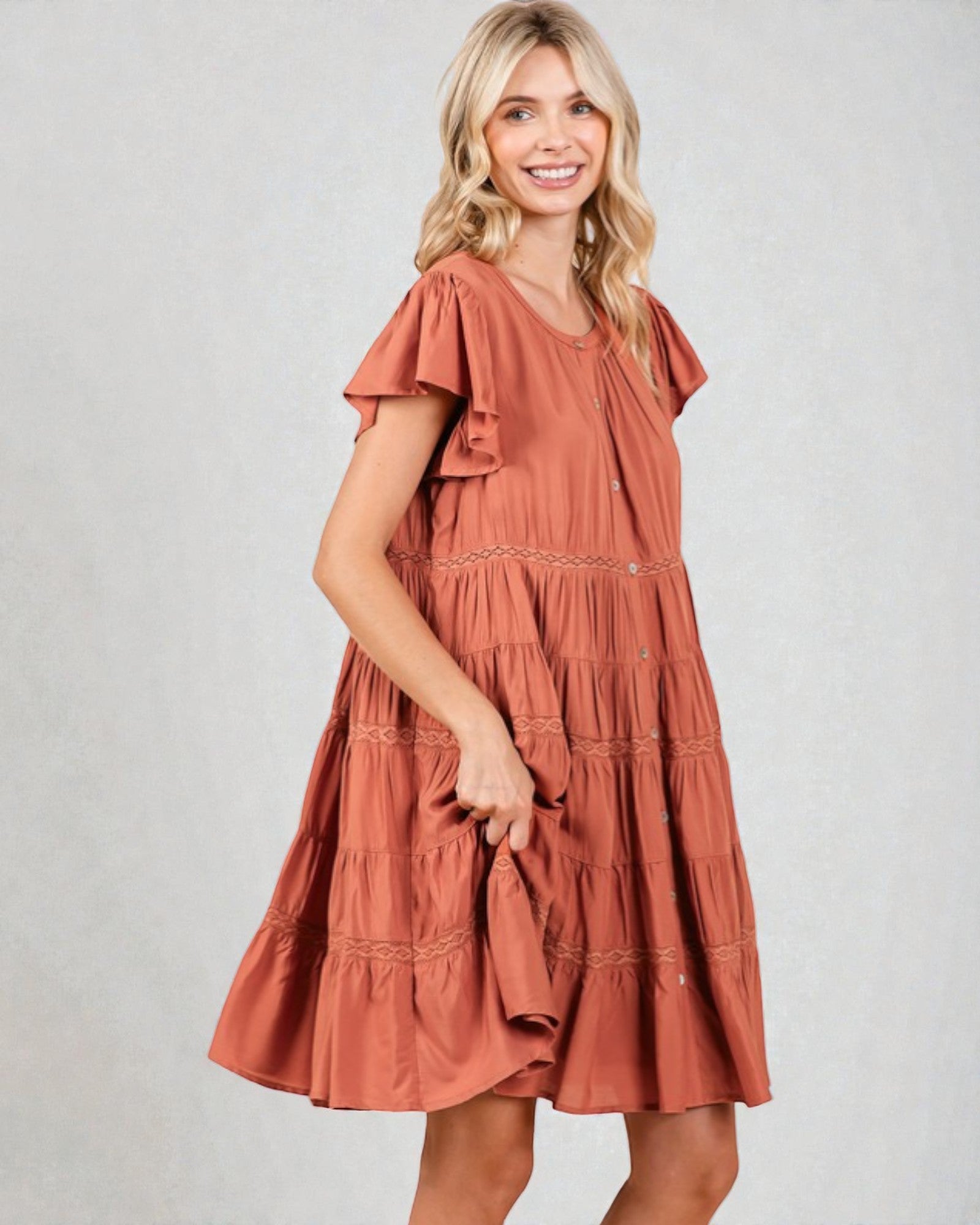 Woman wearing a rust-colored dress with ruffled sleeves on a plain background