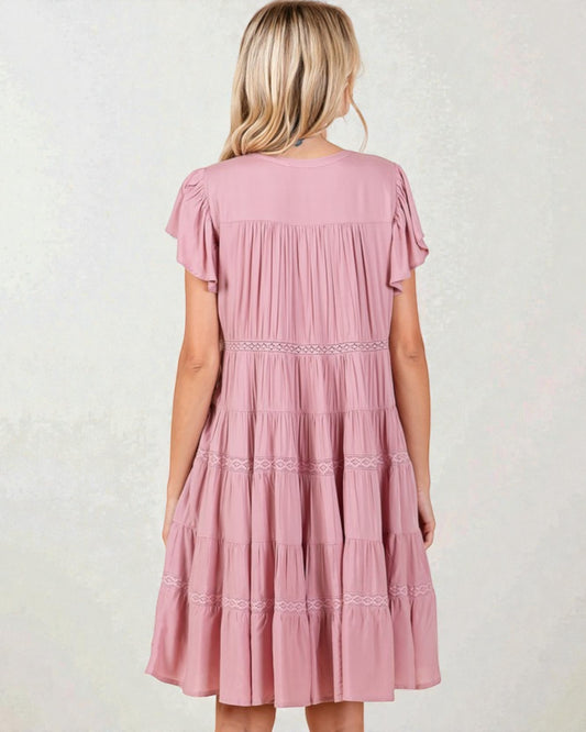 Pink tiered dress worn by a person on a white background