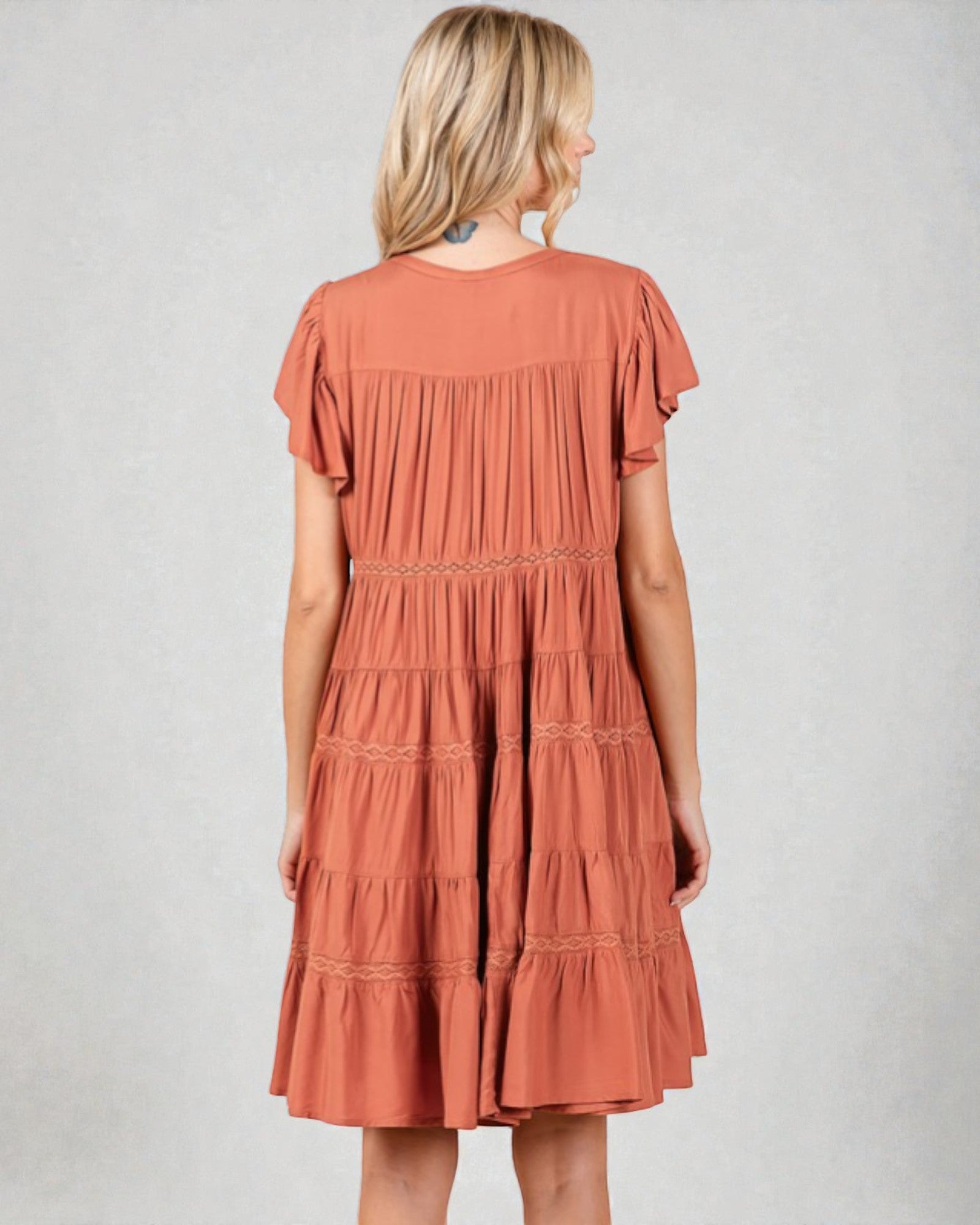 Woman wearing a tiered rust-colored dress on a plain background