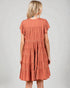 Woman wearing a tiered rust-colored dress on a plain background