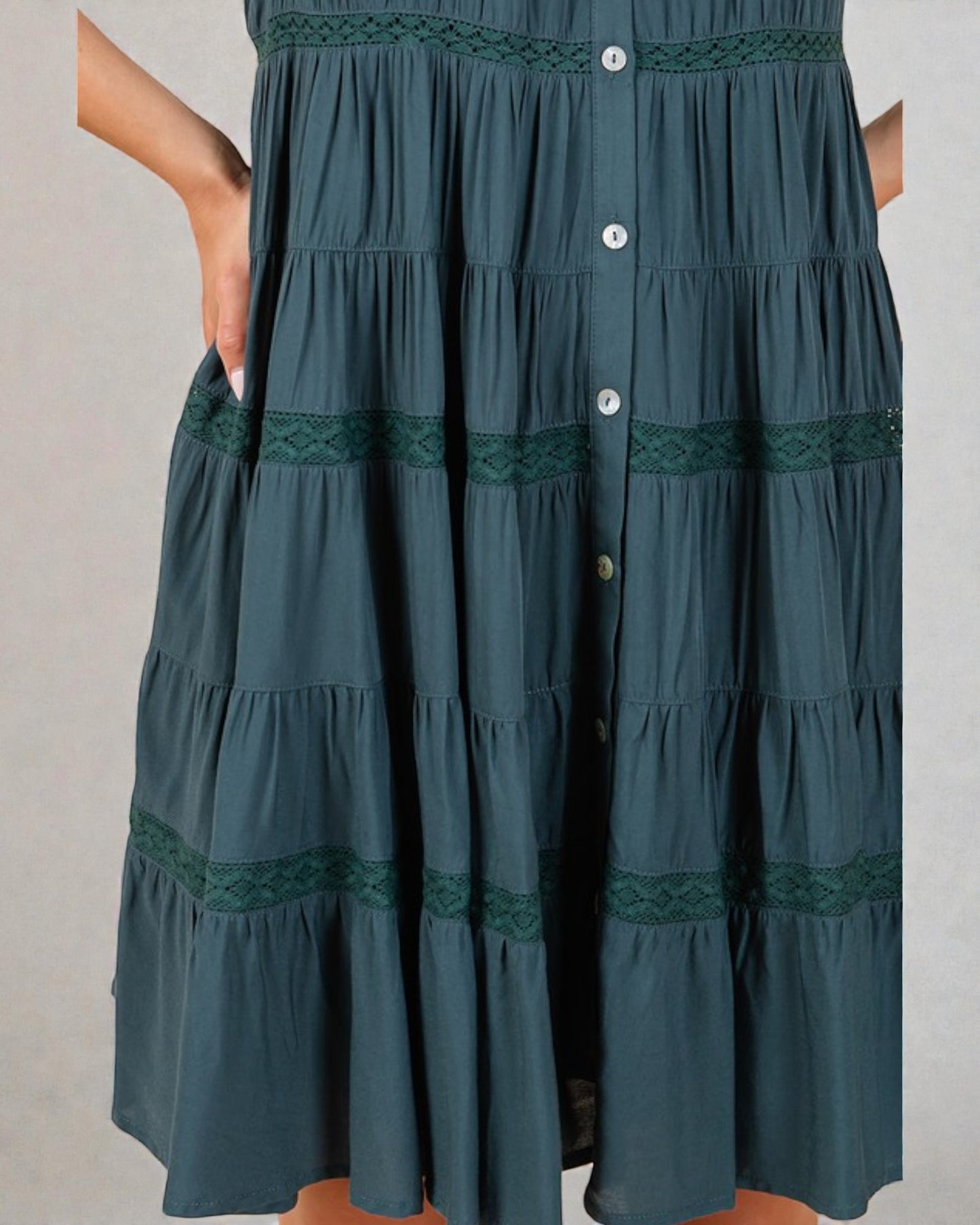 Green tiered dress with lace details on a plain background