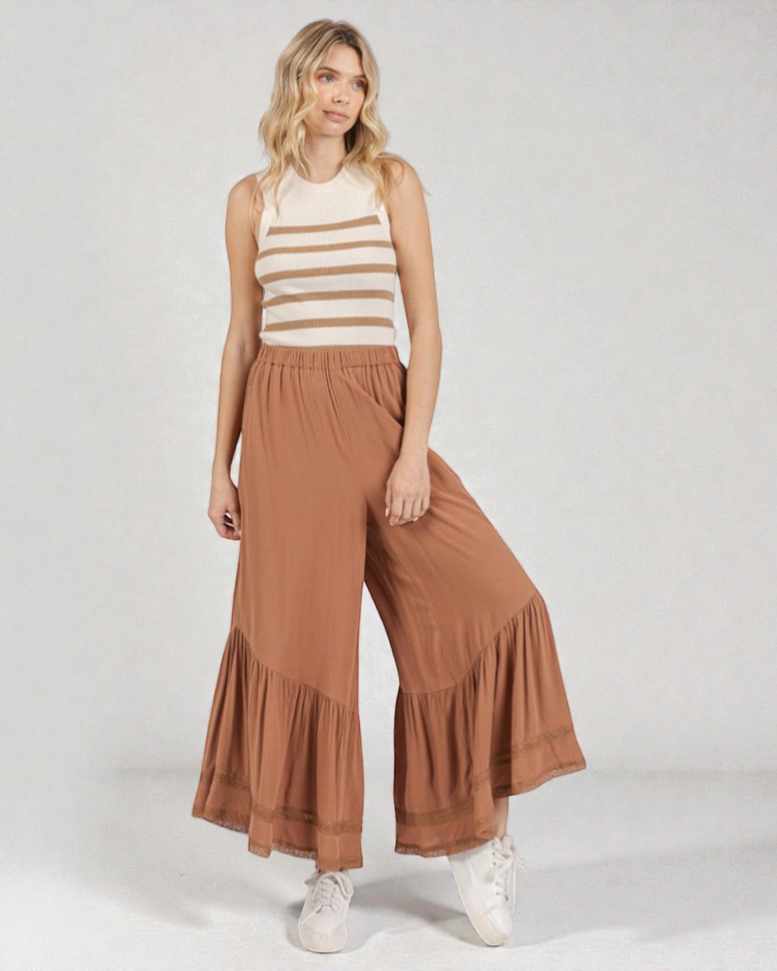 Woman wearing a striped sleeveless top and brown ruffled pants on a white background
