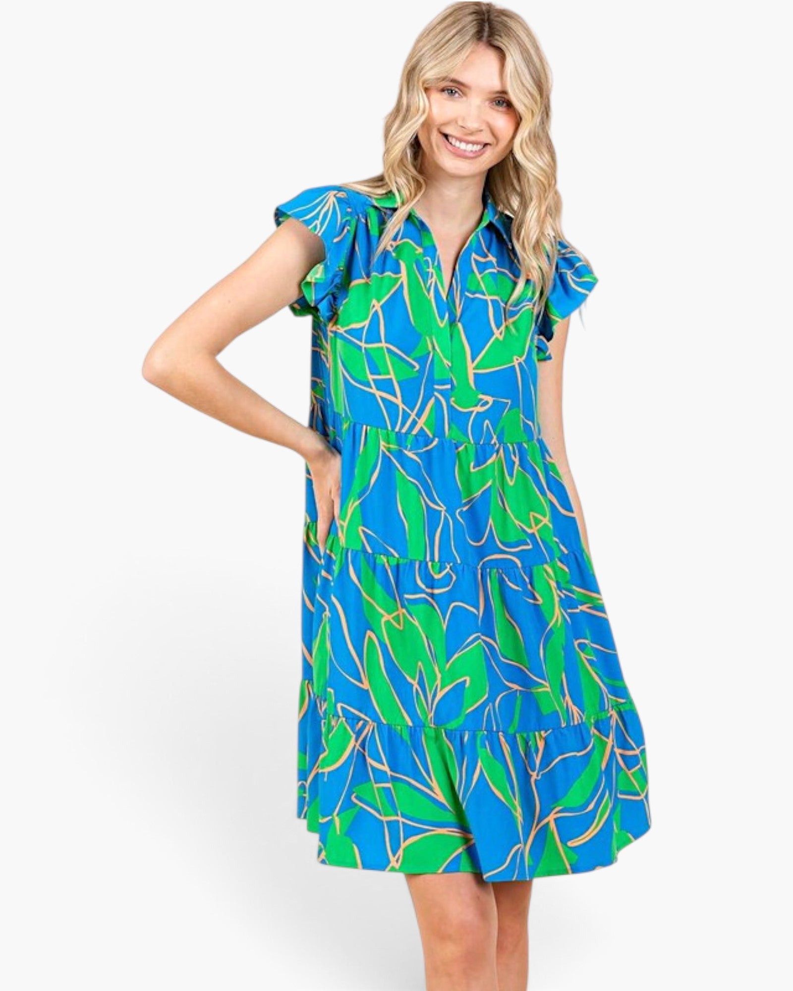 A woman modeling a short-sleeve collared dress with a bright blue and green tropical leaf print, set against a plain white studio background.