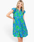 A woman modeling a short-sleeve collared dress with a bright blue and green tropical leaf print, set against a plain white studio background.