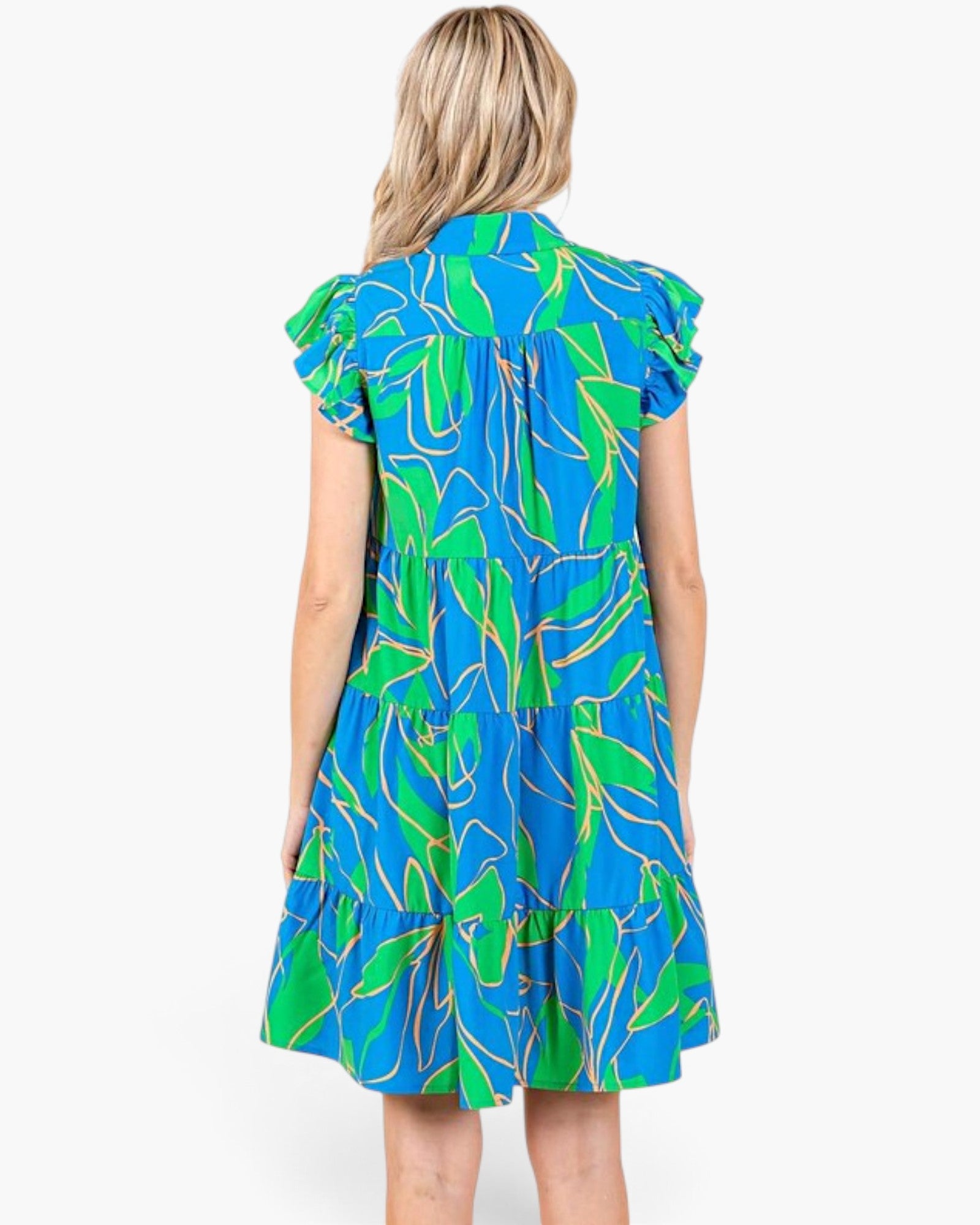 A woman viewed from the back wearing a tiered short-sleeve dress with a bright blue and green tropical leaf print, set against a plain white background.