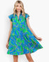 A woman modeling a short-sleeve tiered dress with a vibrant blue and green tropical leaf print outlined in yellow, set against a plain light gray background.