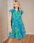 Woman wearing a blue dress with green leaf pattern indoors.