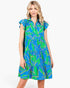 A woman modeling a tiered blue and green tropical print dress with flutter sleeves and a ruffled collar, set against a plain white studio background.