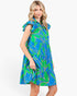 A woman modeling a sleeveless tiered dress with a vibrant blue and green tropical leaf print, set against a plain white studio background.