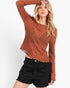 A woman modeling a textured, long-sleeve cropped top in a rust orange color, paired with black distressed denim shorts, against a plain white background.