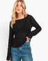 A woman modeling a black textured, semi-sheer long-sleeve top with a smocked chest panel, paired with blue jeans, against a plain white background.