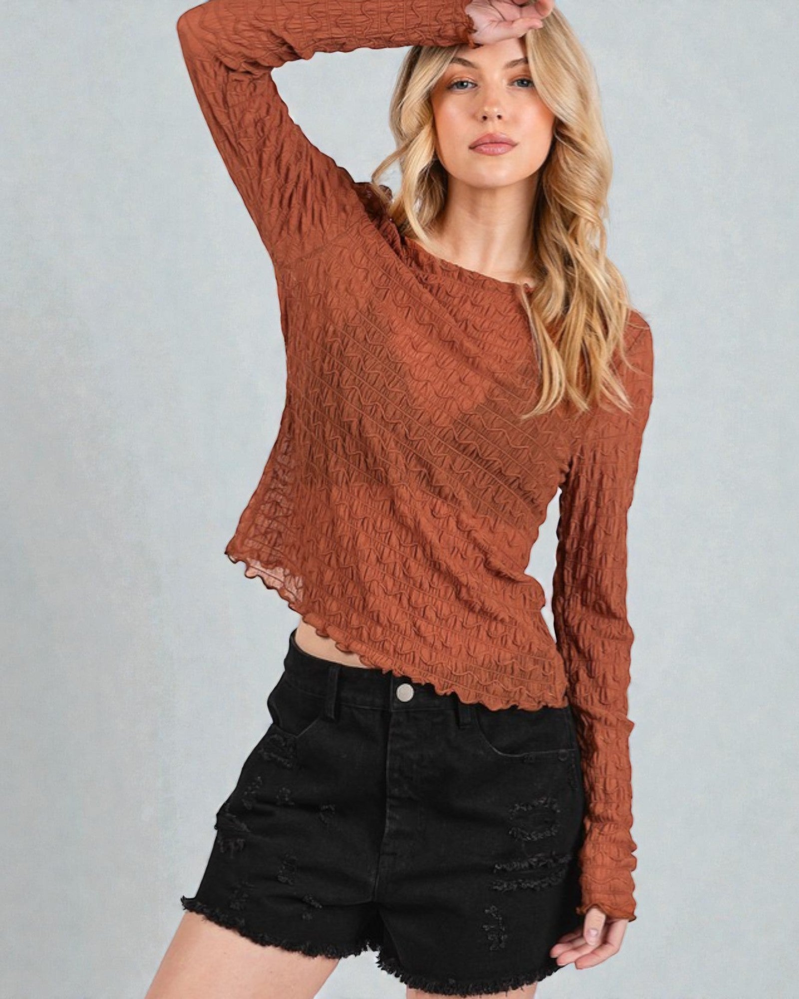 Woman wearing a brown textured sweater and black shorts on a gray background