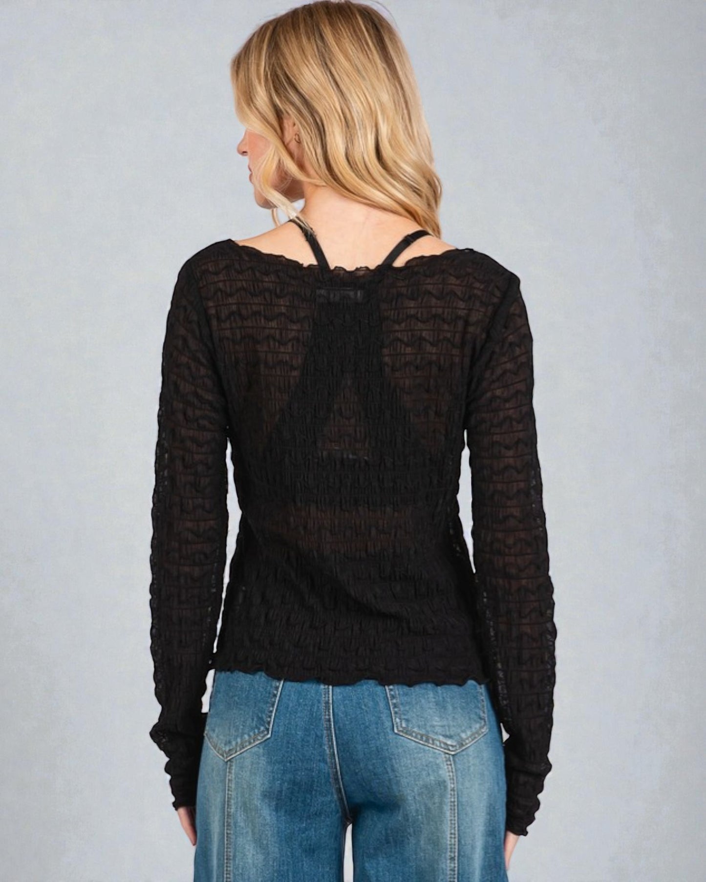 Person wearing a black long-sleeve top and blue jeans on a gray background