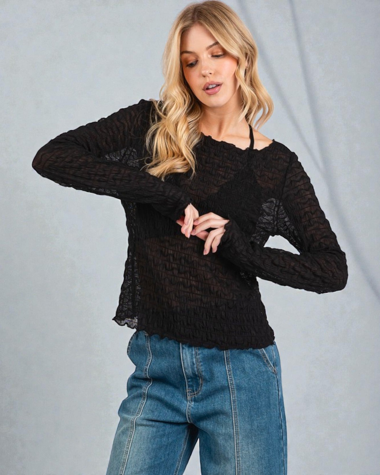 Woman wearing a black textured sweater and blue jeans against a gray background
