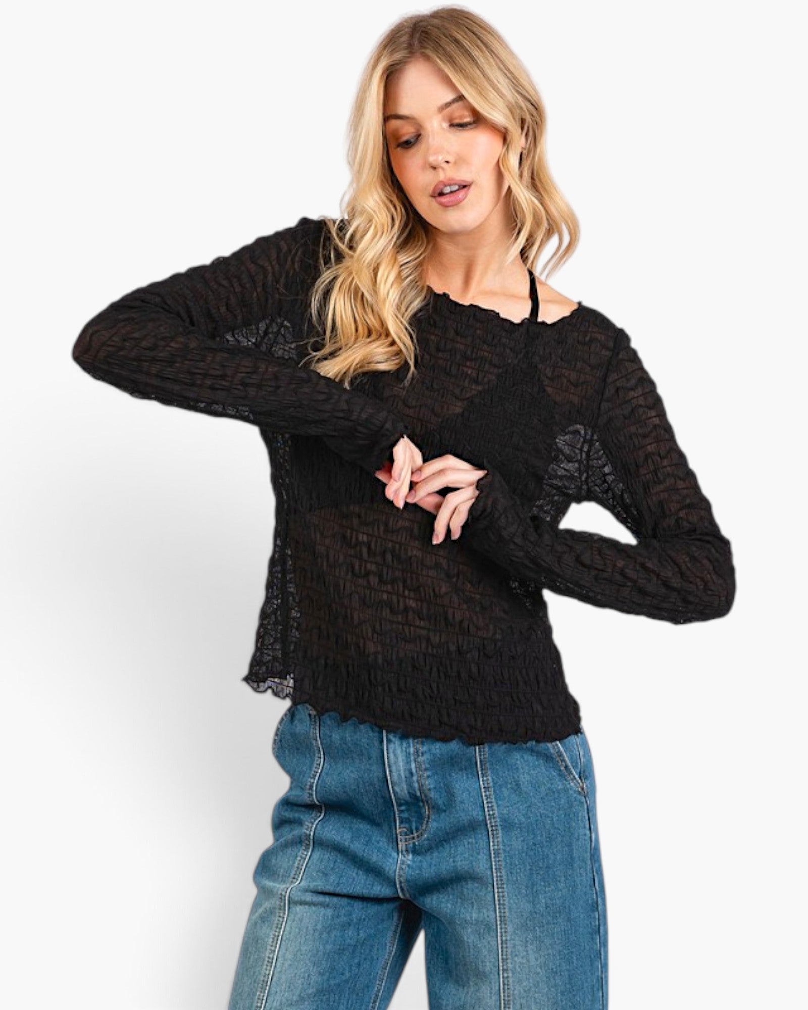 A woman wearing a black long-sleeve textured knit top with lace details and blue jeans, photographed against a clean white studio background.