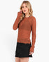 A woman modeling a textured, long-sleeve crewneck sweater in a rust orange color, paired with a black distressed denim mini skirt, against a plain white studio background.