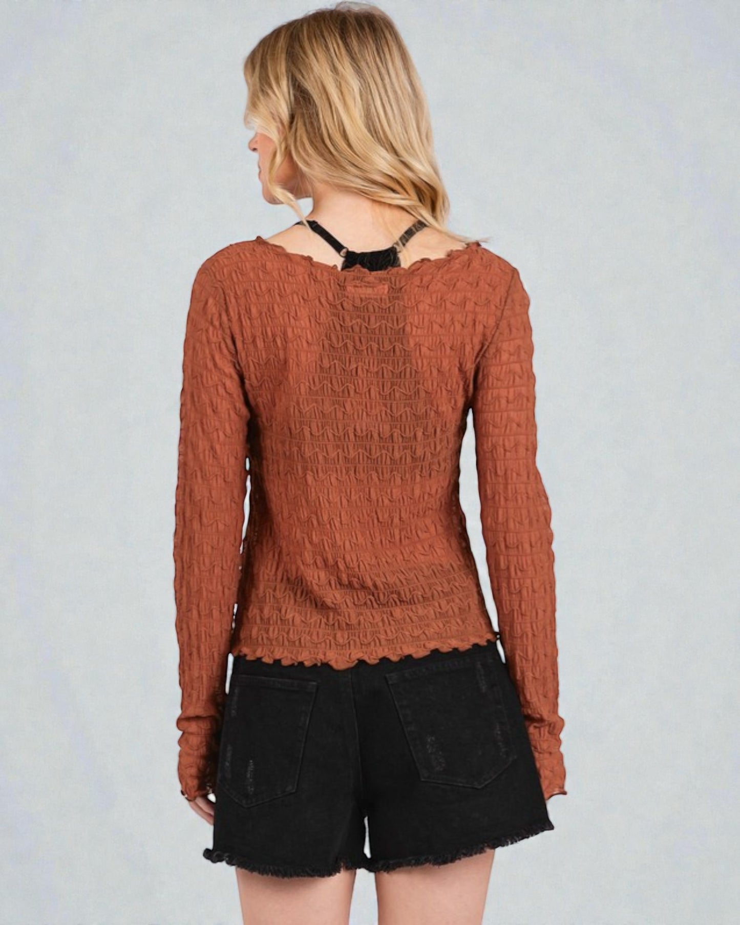 Person wearing a brown textured sweater and black shorts on a light gray background