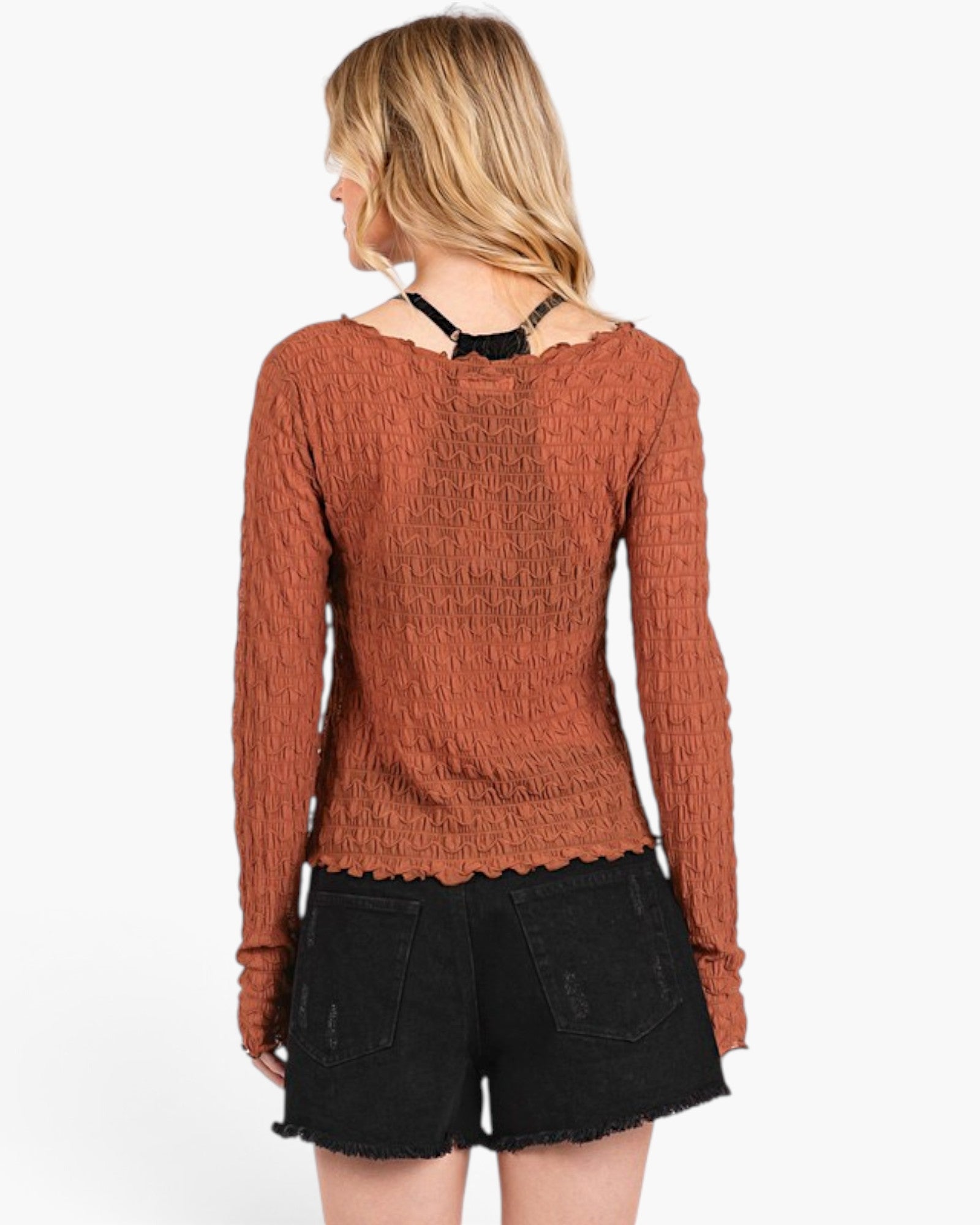 A woman shown from the back wearing a textured rust-orange long-sleeve top with a black lace-up back detail and black denim shorts, against a plain white background.