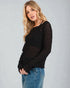 Woman wearing a black sweater with sheer sleeves against a gray background