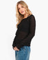 A blonde woman wearing a black textured knit long-sleeve top with a crew neck and blue jeans, photographed against a plain white studio background.