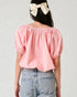 Person wearing a pink off-shoulder top and blue jeans with a white bow in hair on a light gray background