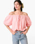 A woman wearing a light pink off-the-shoulder puff-sleeve top with a drawstring tie at the neckline, paired with light-wash blue jeans, against a plain white background.
