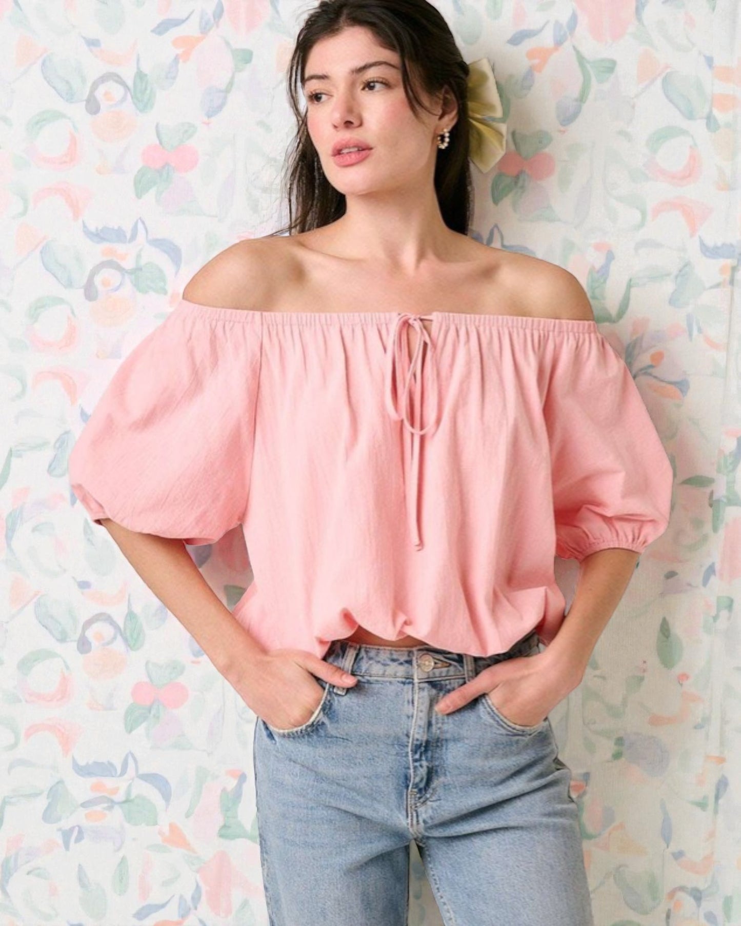 Woman wearing a pink off-shoulder top and blue jeans against a colorful abstract background