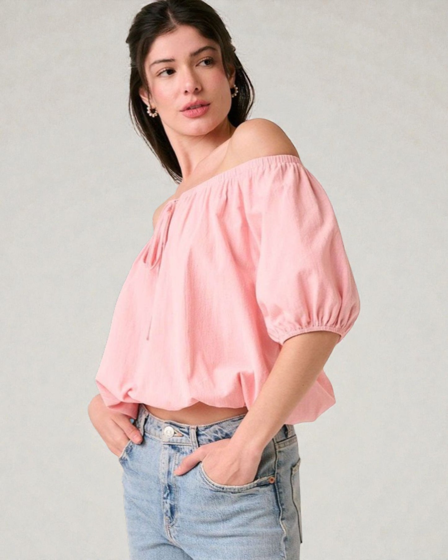 Woman wearing a pink off-shoulder top and blue jeans on a plain background