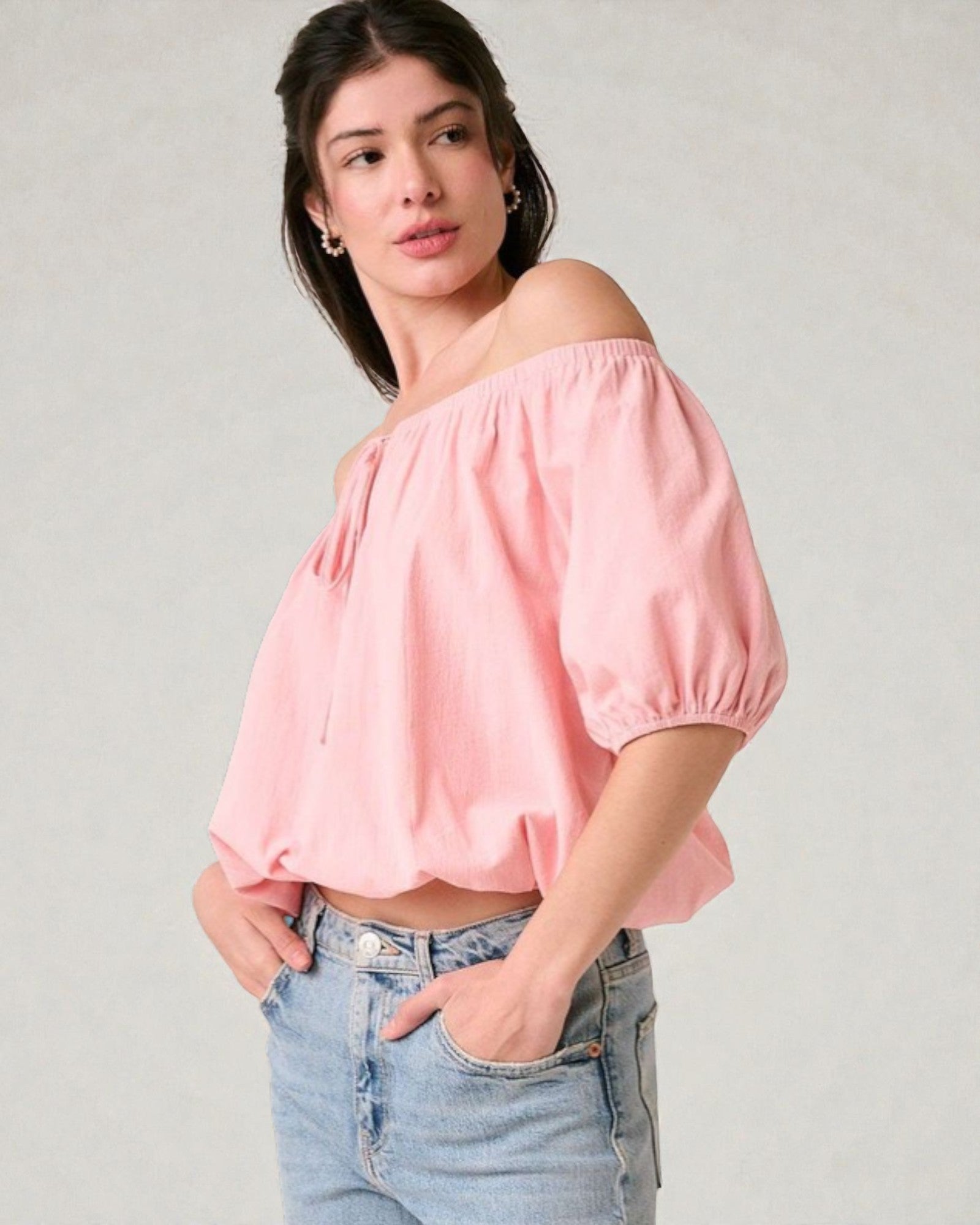 Woman wearing a pink off-shoulder top and blue jeans on a plain background