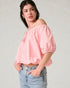 Woman wearing a pink off-shoulder top and blue jeans on a plain background